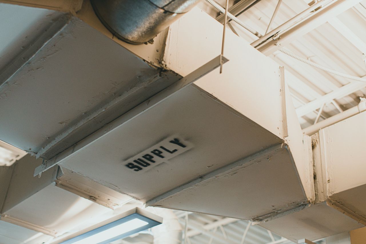 hero-img-02 Close-up view of an air duct labeled 'SUPPLY' in an industrial setting.