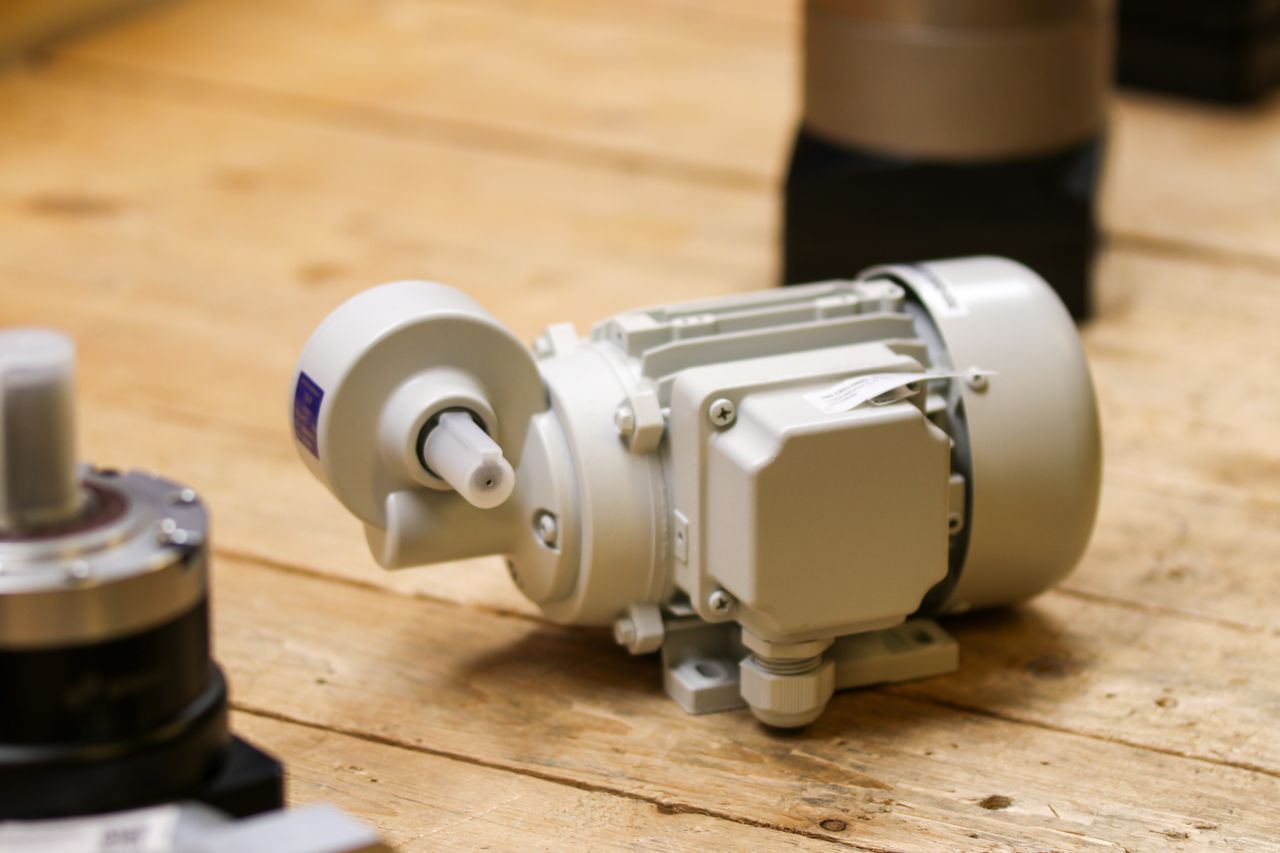 services-03 Close-up of a white industrial motor placed on a wooden surface inside a workshop.
