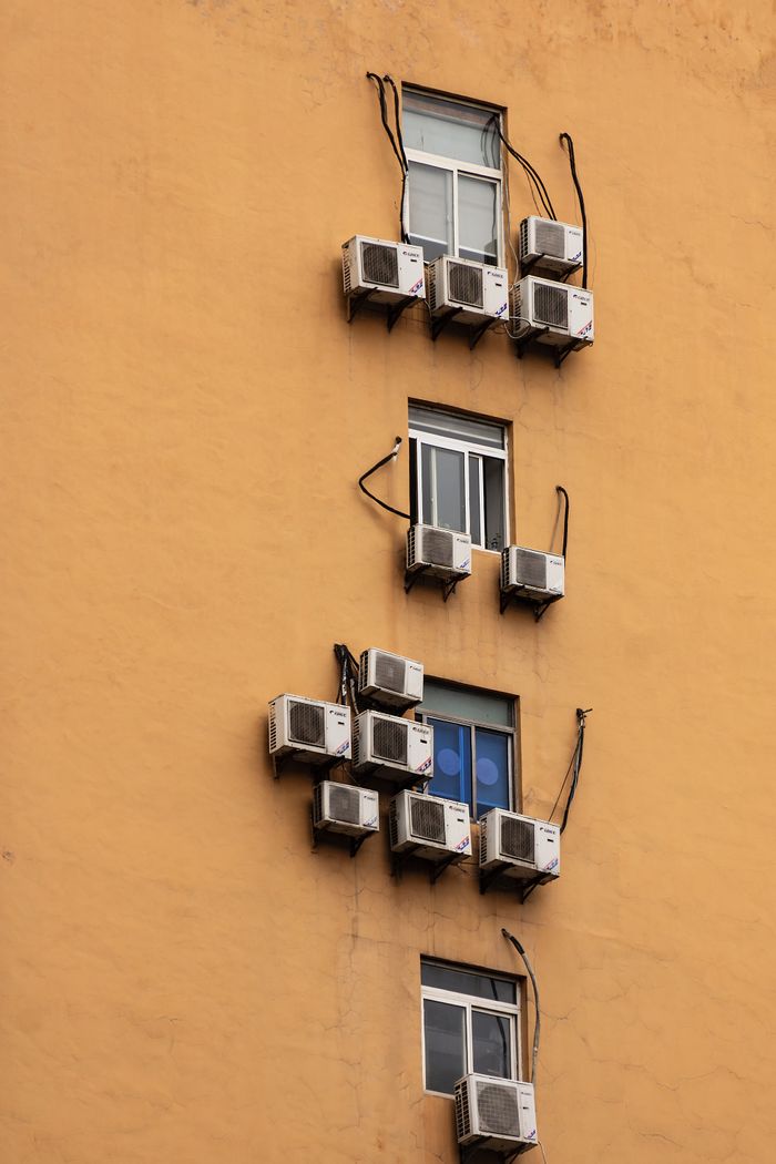 gallery-2 Yellow building facade with windows and numerous air conditioning units attached.