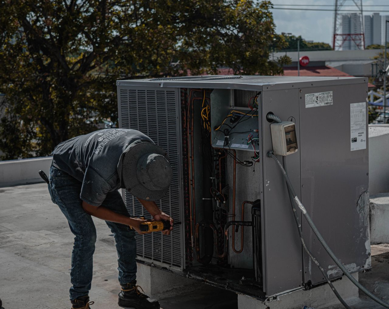 gallery-1 A technician is repairing an air conditioning unit on a rooftop, demonstrating skilled manual work.