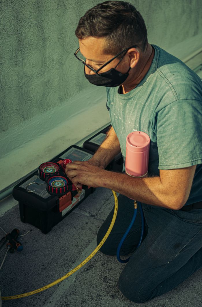 services-01 A technician kneels outdoors, performing HVAC maintenance using specialized tools, enhancing system performance.
