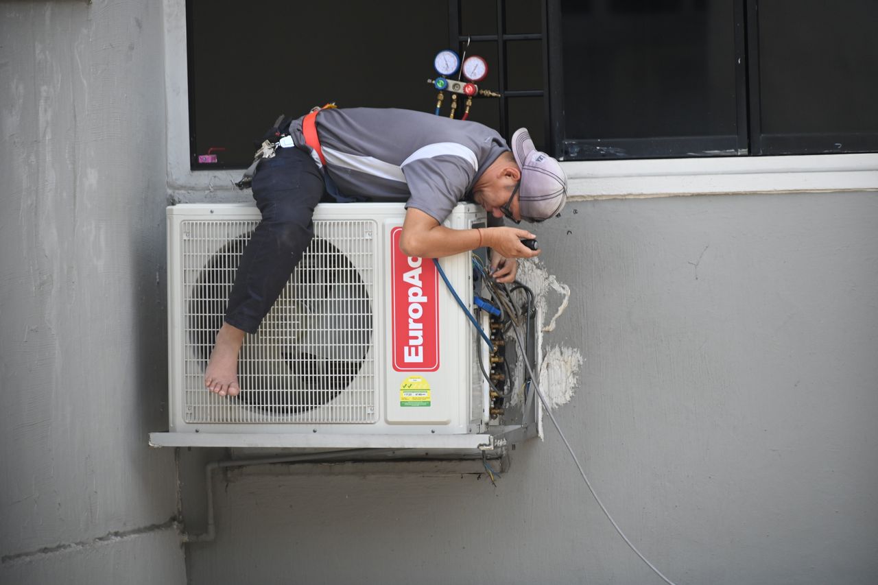 services-img A technician skillfully repairing an outdoor air conditioning unit mounted on a building wall.